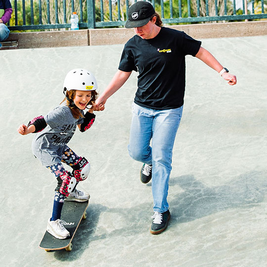 Girl skateboarding with man helping her balance