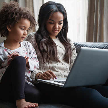 Two sisters sitting on sofa using laptop