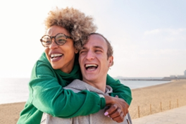 Woman and man laughing together holding each other at the beach